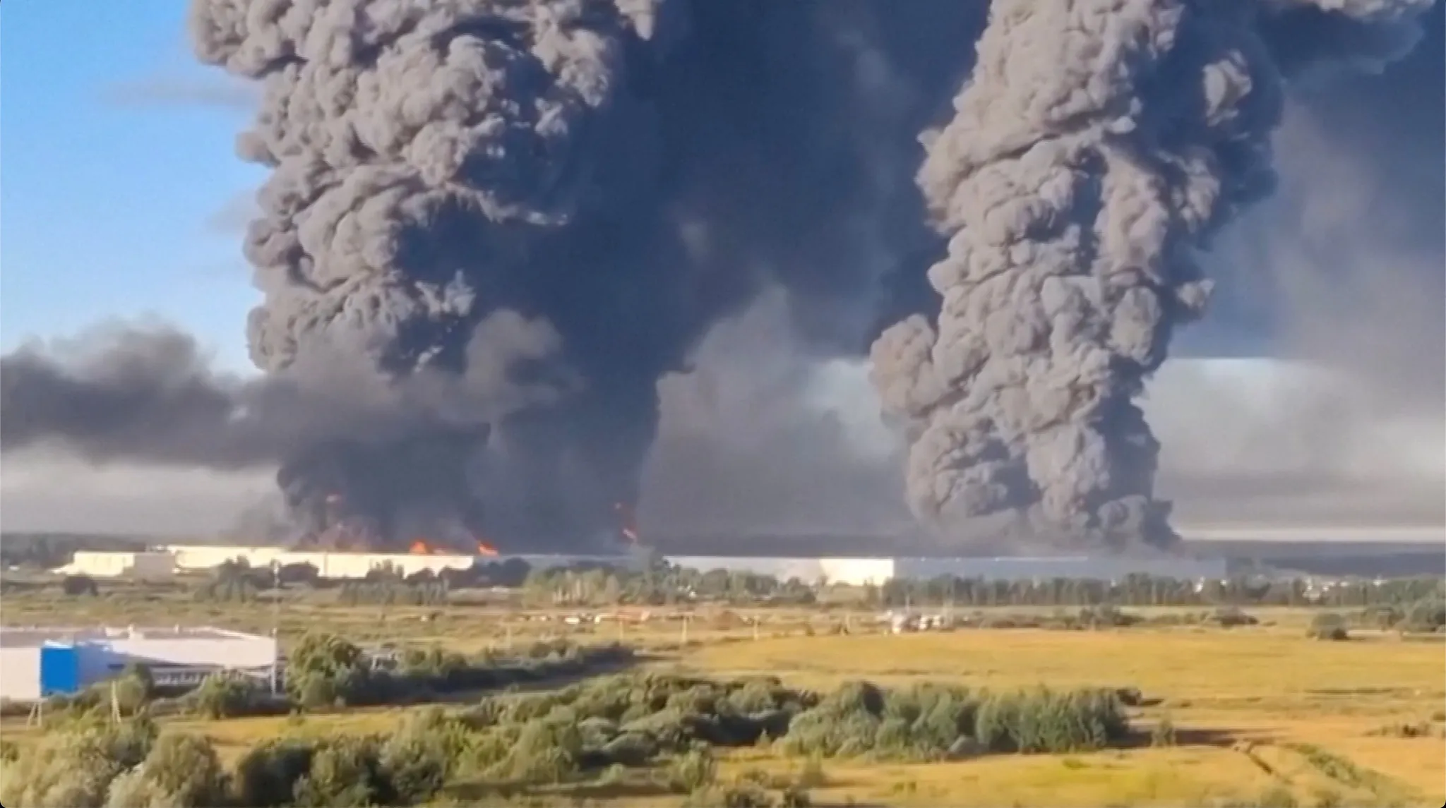 Smoke rising from a large Wildberries logistics warehouse with emergency vehicles near the building