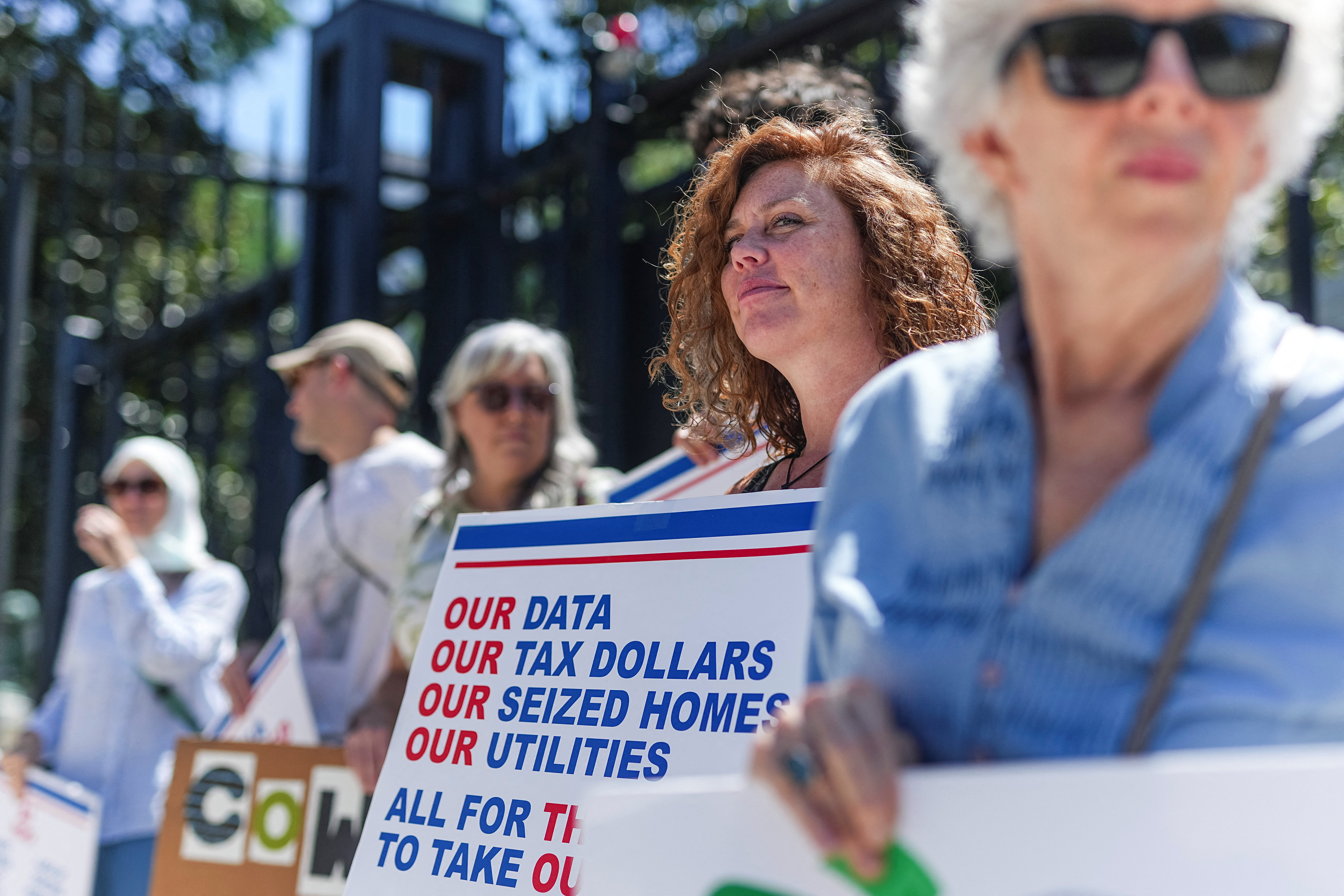 A large crowd of protesters holding signs marches in a street demonstration against AI data centers